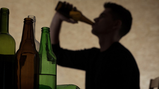 Im Hintergrund von mehreren Flaschen trinkt eine Person aus einer Flasche